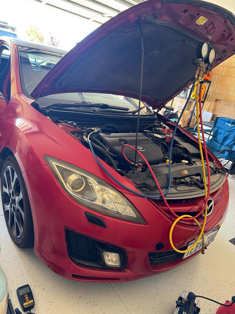 Red Mazda with air conditioning gauges connected under the open bonnet